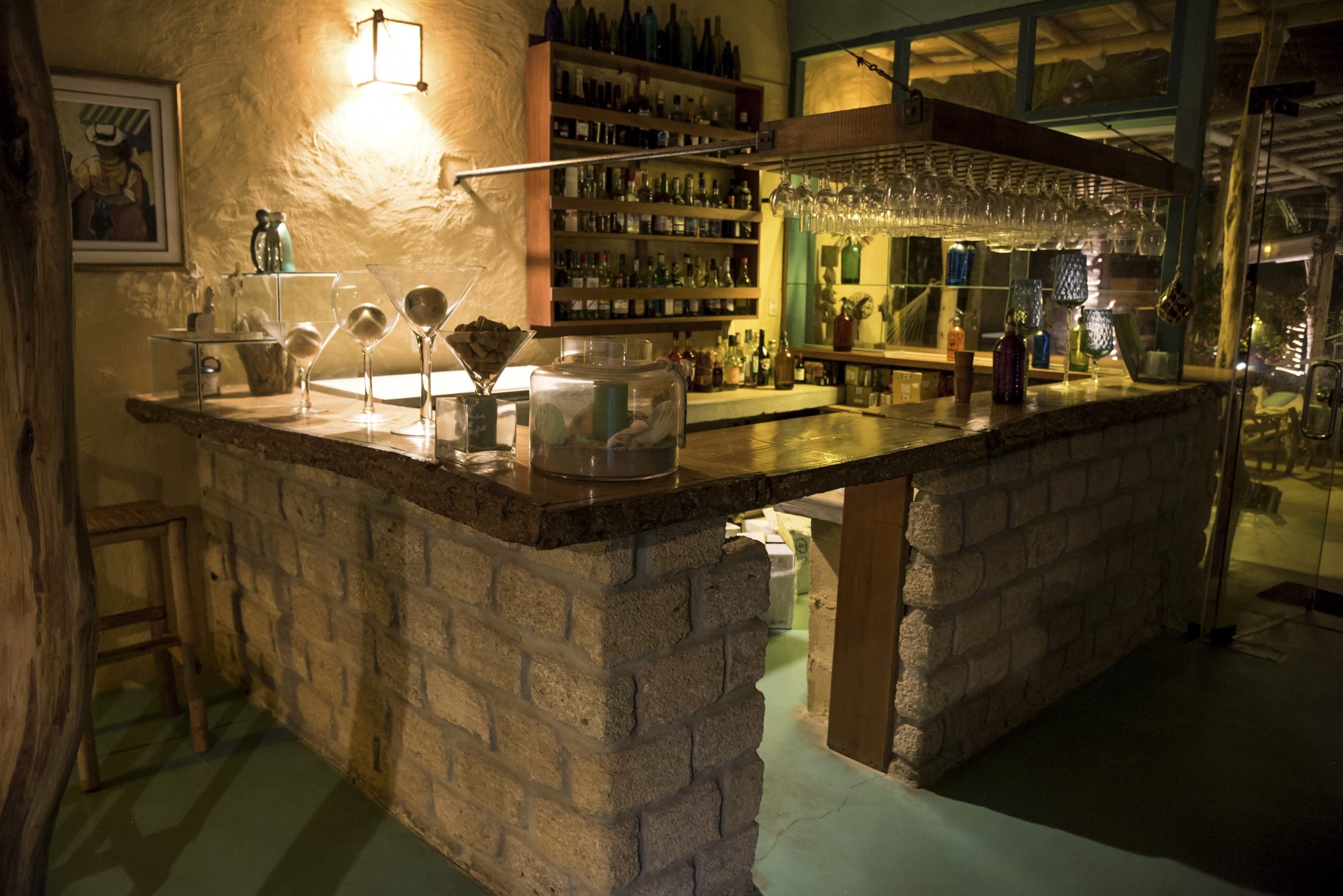 A bar area with a stone counter, shelves with bottles, and a hanging glass rack.