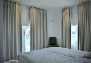 Une chambre d’hôtel avec un grand lit, deux fenêtres avec des rideaux, une chaise et un luminaire au plafond.