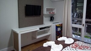 Une chambre d’hôtel équipée d’un téléviseur fixé au mur, d’une machine à café, d’une petite étagère avec des verres et d’une fenêtre avec des rideaux.
