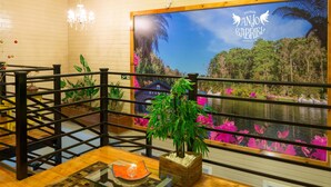 L’intérieur d’un restaurant avec un plancher en bois, une grande fresque représentant un paysage tropical, une plante en bambou et une table en verre sur laquelle est posée une bougie.