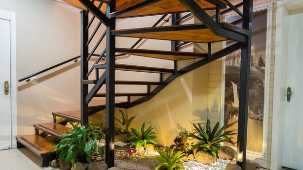 Un escalier moderne avec des marches en bois et des rampes en métal, entouré de plantes en pot et de rochers.