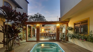 Ein Pool mit Pergola und Essbereich im Hintergrund.