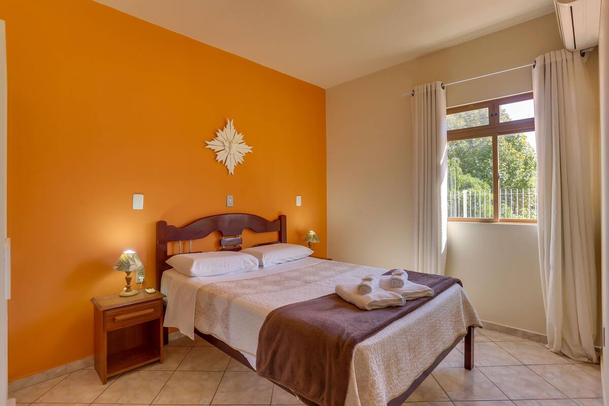 Una camera d'albergo con un letto, un comodino, una lampada e una finestra con tende.
