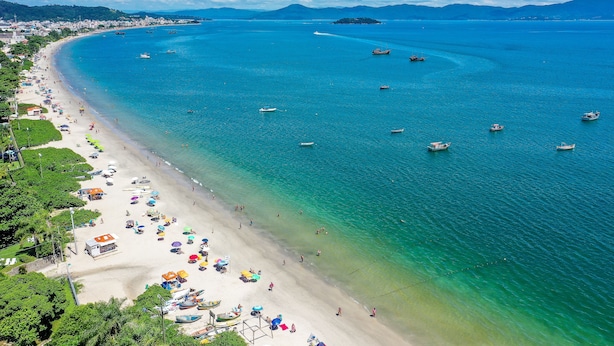 Ein Küstenstrand mit klarem türkisblauem Wasser, Booten und Strandsonnenschirmen.
