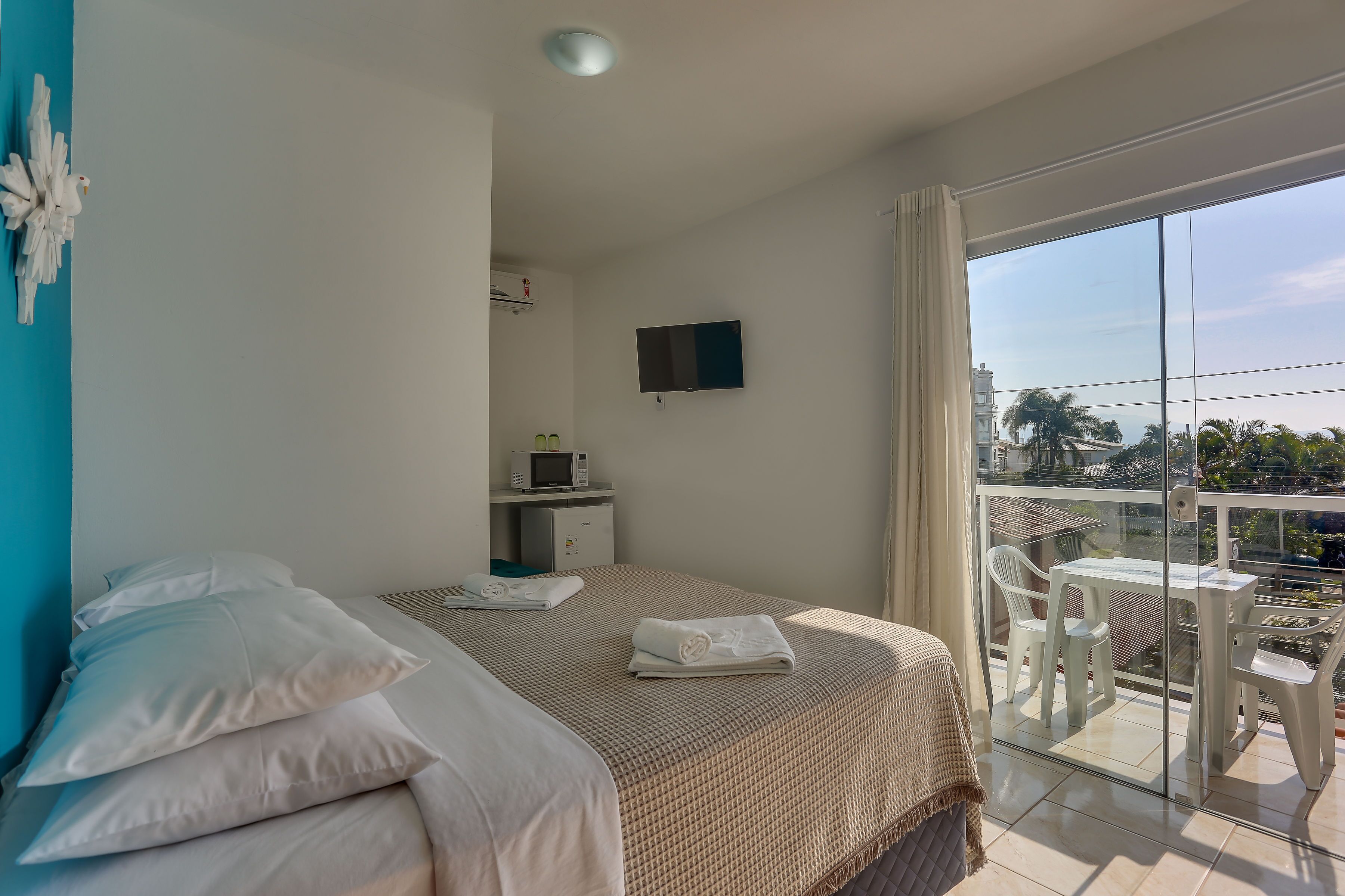 Une chambre d’hôtel avec un lit, une télévision, un balcon avec une table et des chaises, et une vue sur la ville.