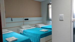 A hotel room with two beds, each with a blue bedspread and white pillows. There is a control panel on the wall and a window with a curtain. - Lider Hotel (São Bernardo do Campo)