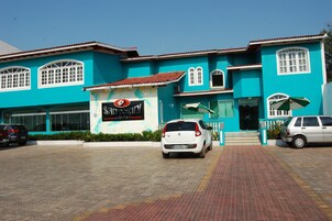 Um hotel com fachada turquesa, amplas janelas e uma placa.
