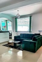 Uma sala de estar moderna com um sofá verde escuro, uma mesa de centro de vidro e um lustre.