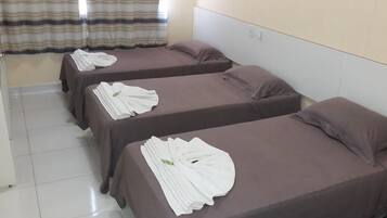 Habitación de hotel con dos camas, cada una con una toalla blanca doblada con cuidado y una almohada marrón.