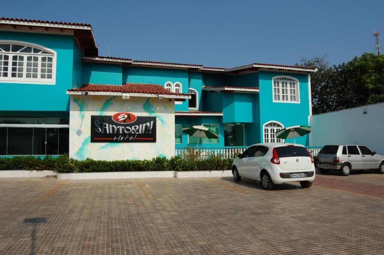 A hotel with a turquoise facade, a signboard, and two cars parked in front.