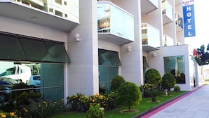 A modern hotel with a glass facade, multiple balconies, and a well-maintained garden with various shrubs and flowers. - Itaparica Praia Hotel (Vila Velha)