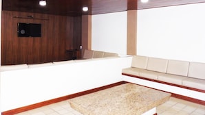 A modern living room with a wooden ceiling, a flat-screen TV mounted on the wall, a beige sofa, and a small coffee table. - Itaparica Praia Hotel (Vila Velha)
