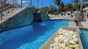 A pool with clear blue water, a stone bridge, and palm trees in the background.