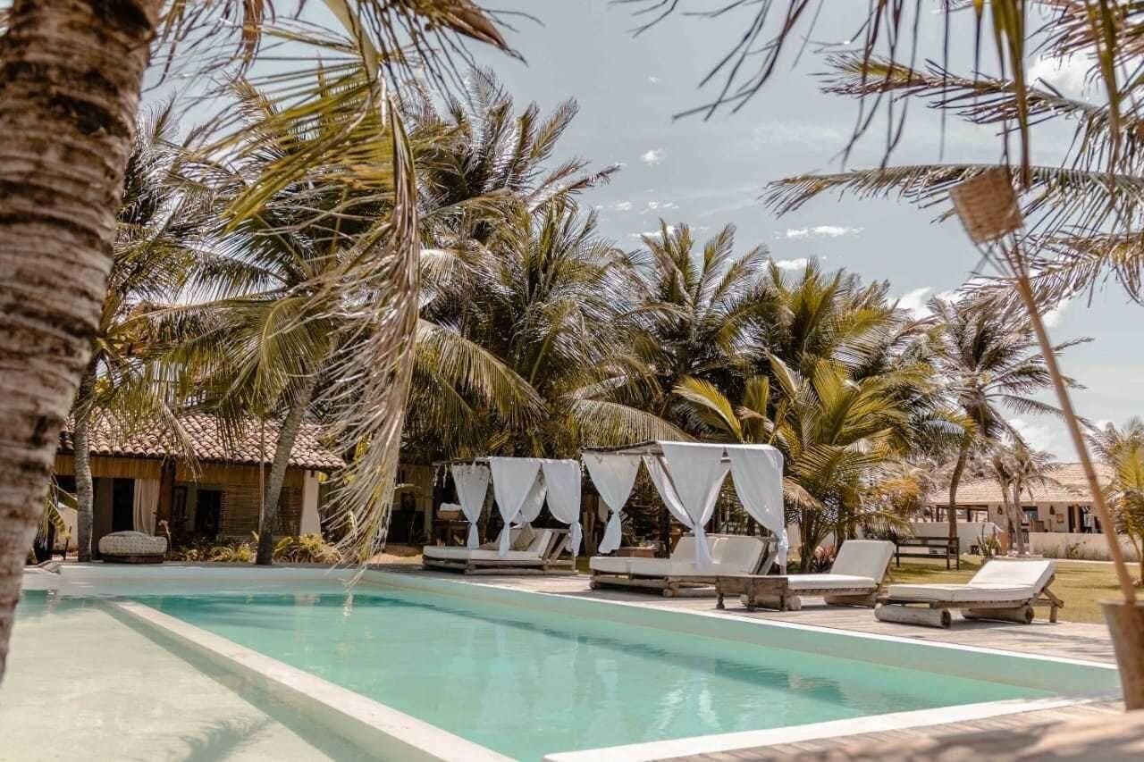 A pool area with lounge chairs and a cabana, surrounded by palm trees and a building with a tiled roof.