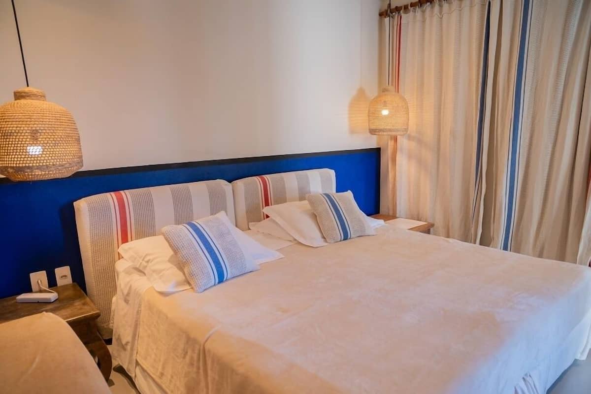 Una habitación de hotel con una cama grande, dos mesitas de noche y dos lámparas colgantes.