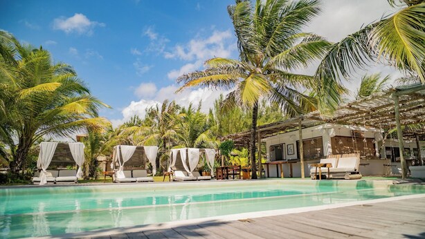A poolside area with lounge chairs and a cabana, surrounded by palm trees. - Zebra Boutique Hotel (Beberibe)