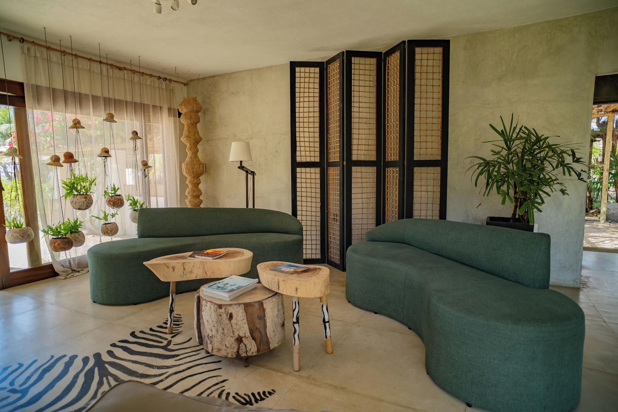 Un salon moderne avec des canapés verts, des tables d’appoint en bois et des plantes suspendues.