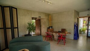 A spacious living area with a large green sofa, a wooden dining table with red chairs, a potted plant, and a wooden cabinet. - Zebra Boutique Hotel (Beberibe)