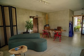 A spacious living area with a large green sofa, a wooden dining table with red chairs, a potted plant, and a wooden cabinet. - Zebra Boutique Hotel (Beberibe)