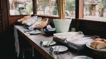 A breakfast buffet setup with various food items and utensils on a wooden table.