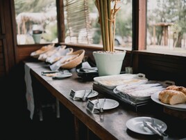 Disposição de buffet de café da manhã com diversos alimentos e utensílios em uma mesa de madeira.