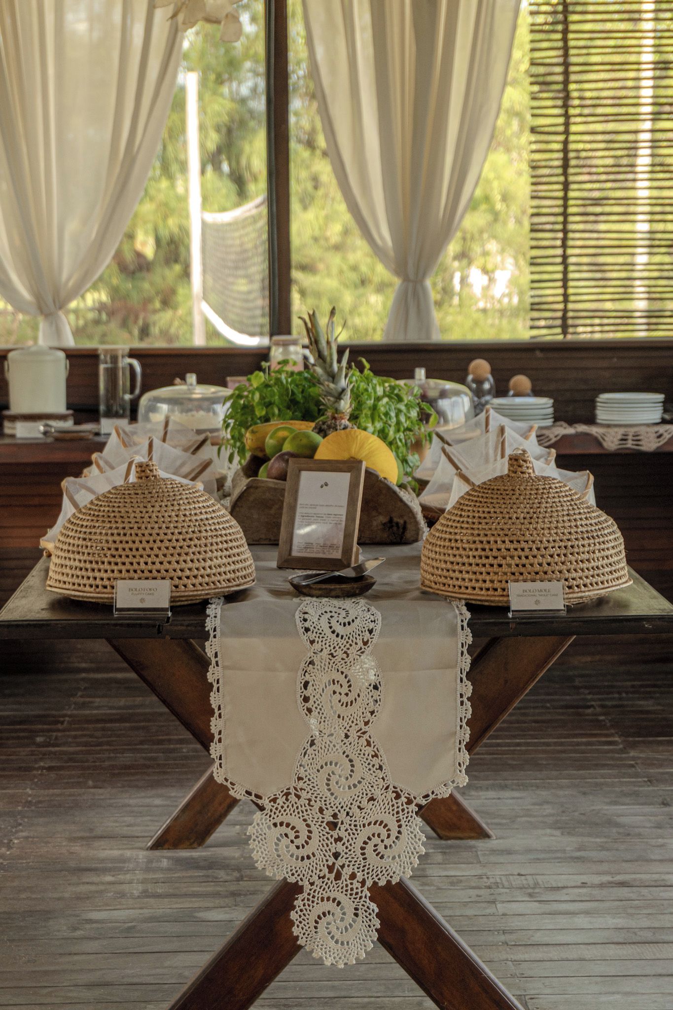 Una mesa con dos lámparas tejidas, un mantel de encaje y una bandeja de frutas.