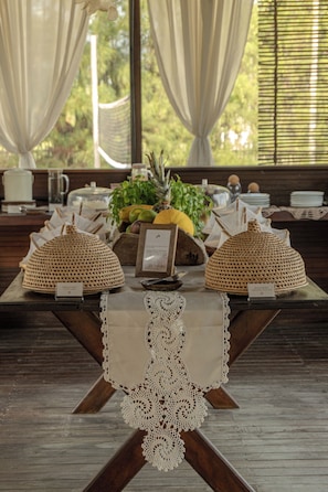 A table set with two woven lamps, a lace table runner, and a fruit display. - Zebra Boutique Hotel (Beberibe)