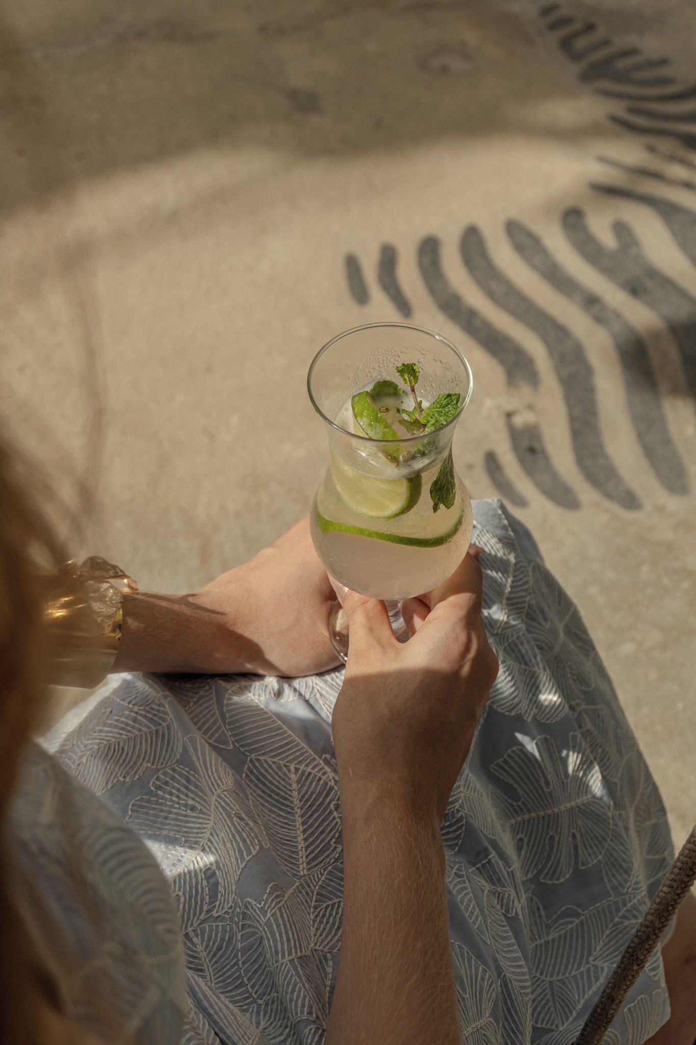 Una persona sostiene un vaso transparente con una bebida, posiblemente un cóctel, con lima y menta.