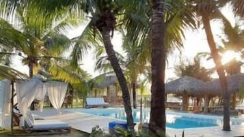 A pool area with palm trees, a grassy area, and a thatched structure.