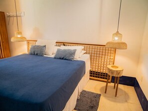 A neatly made bed with a blue bedspread and white pillows, two hanging lamps with woven shades, and a small wooden stool with a round top. - Zebra Boutique Hotel (Beberibe)