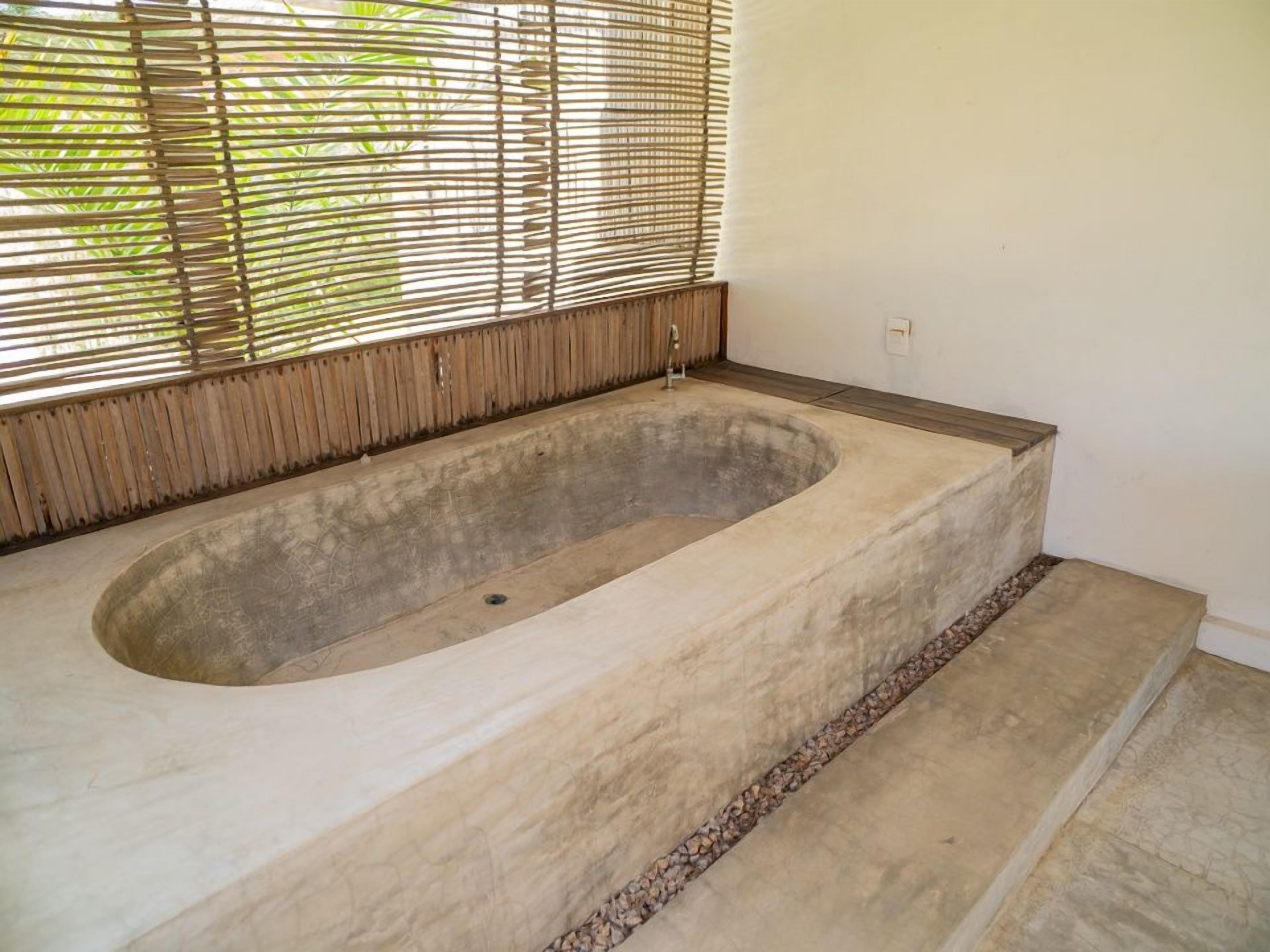 A large freestanding bathtub with a concrete interior and a wooden ledge.
