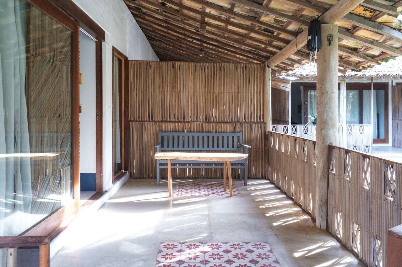 Un espacio al aire libre cubierto con un banco de madera, un muro de bambú y una alfombra estampada.