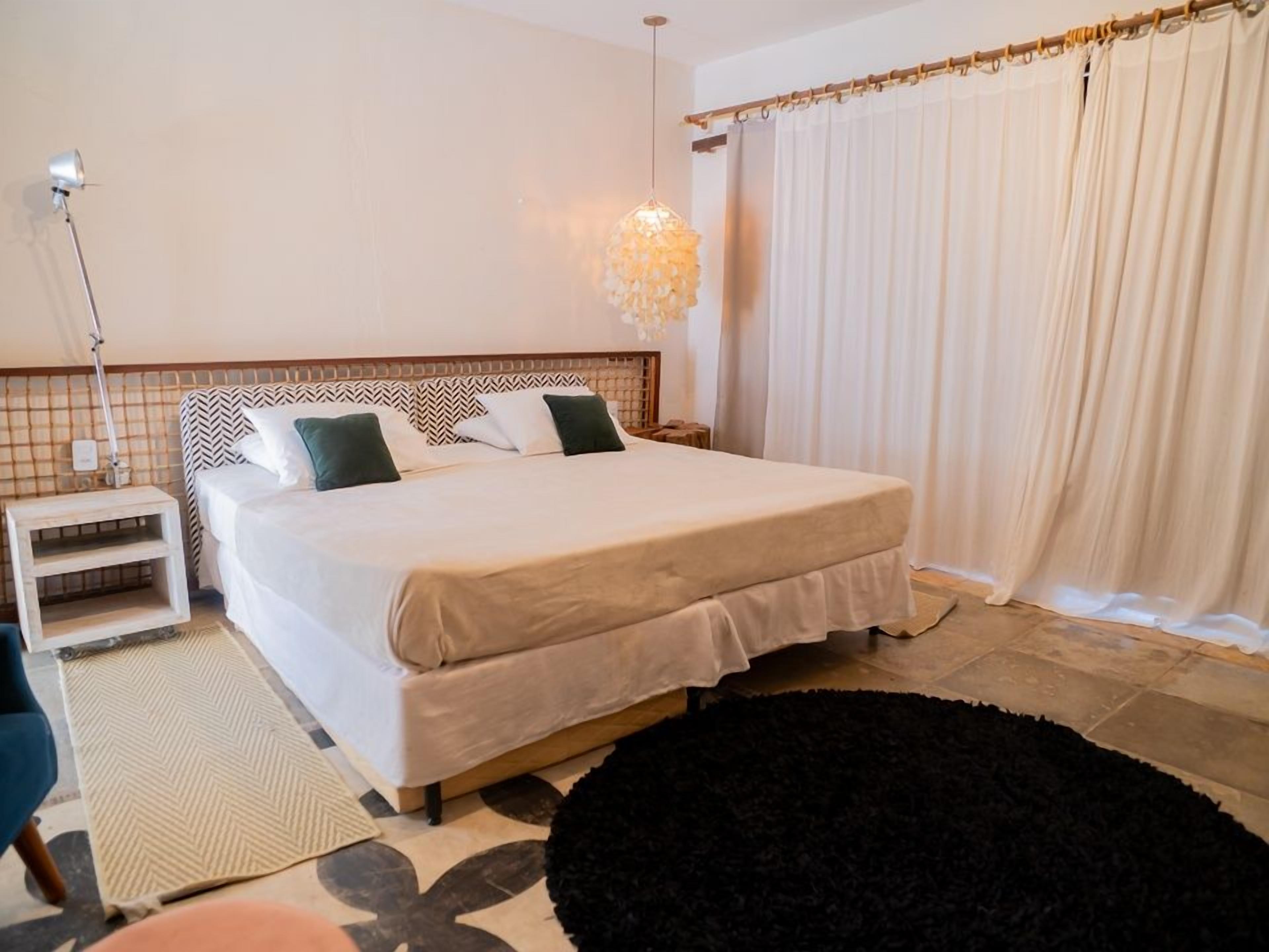 Een keurig opgemaakt slaapkamer met een bed, nachtkastje, lamp en gordijnen.