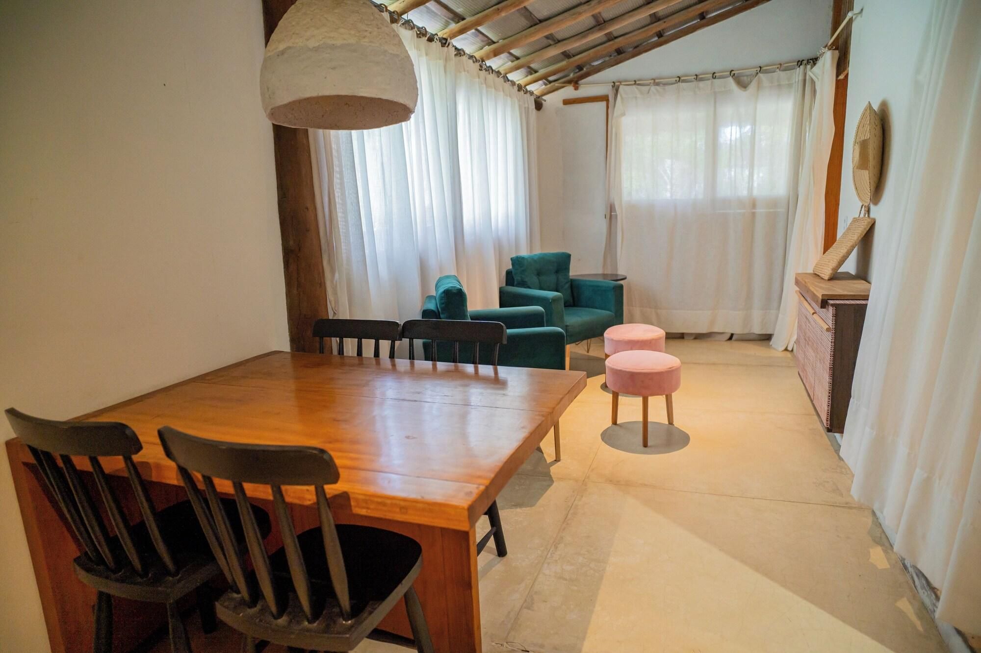 Uma área de refeições com mesa e cadeiras de madeira, luminária pendente e sofá com um banquinho combinando.