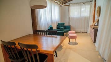 Uma área de refeições com mesa e cadeiras de madeira, luminária pendente e sofá com um banquinho combinando.