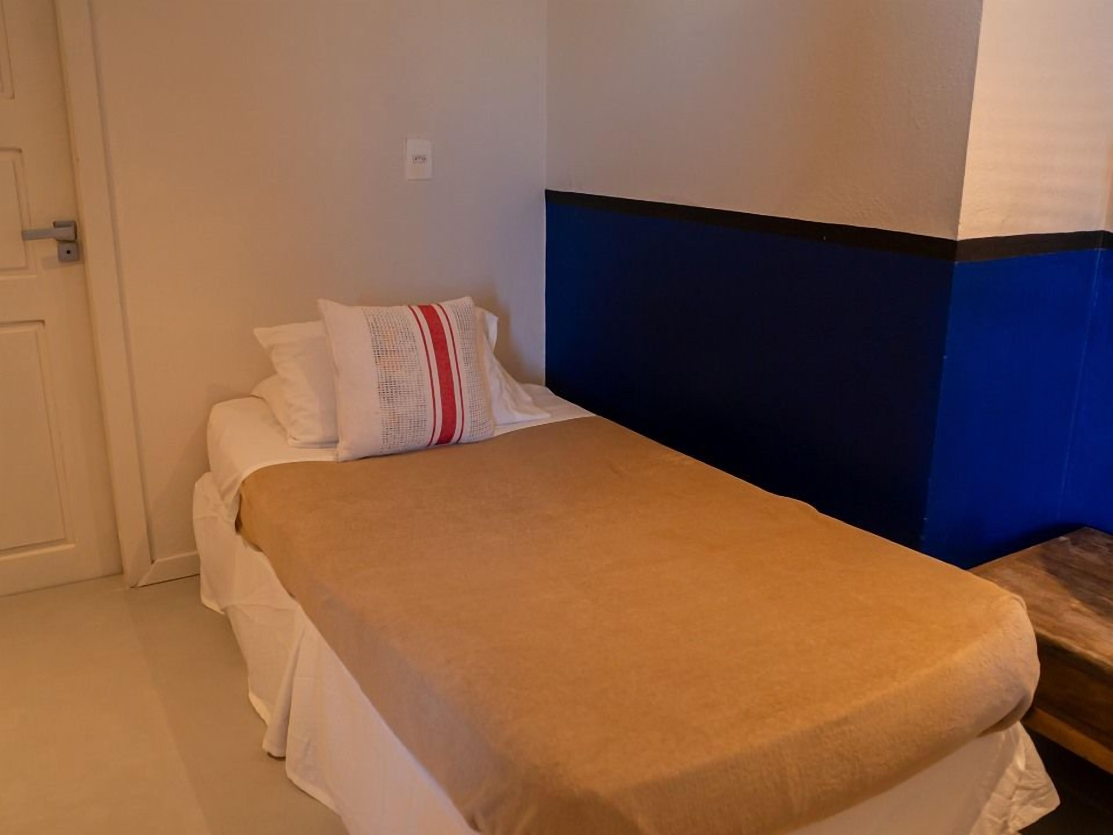 A small, neatly made bed with a beige bedspread and white pillows, a blue and white wall, and a closed door.
