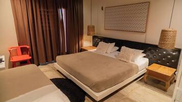 Quarto de hotel com uma cama grande, uma mesa pequena, uma cadeira e uma janela ampla com cortinas.