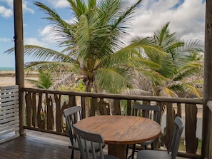 A wooden deck with a round table and chairs, overlooking a beach with palm trees and a cloudy sky. - Zebra Boutique Hotel (Beberibe)