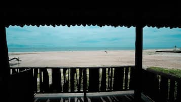 A beach view from a covered area with a wooden railing.