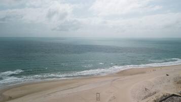 Uma extensa praia de areia com ondas suaves, céu claro e horizonte distante.