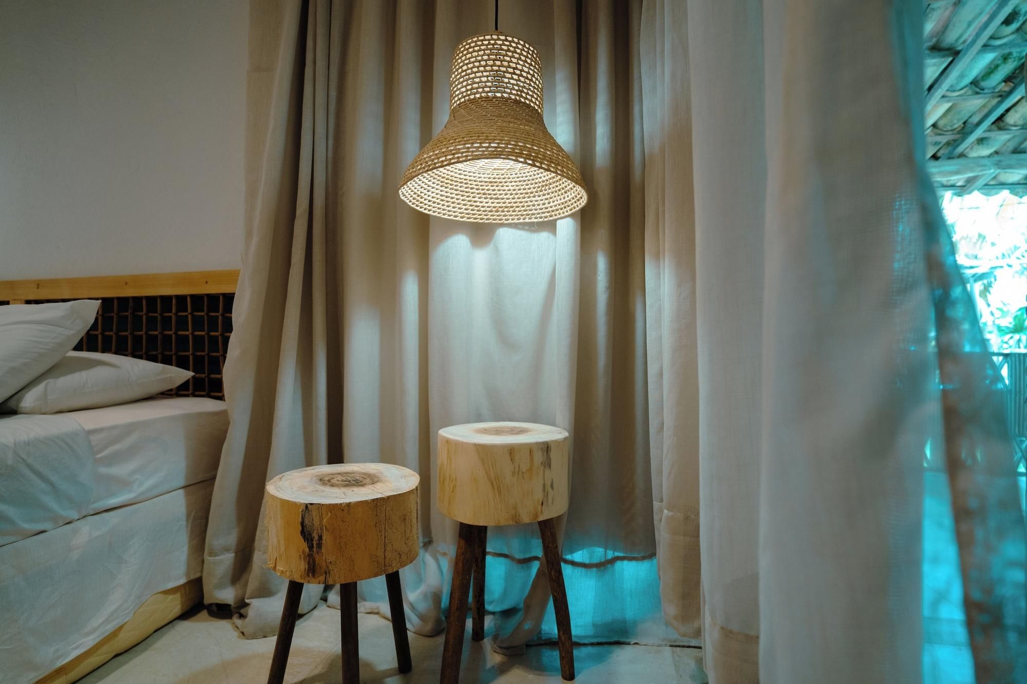A bedroom with a bed, two stools, and a hanging light fixture.