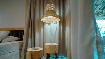 A bedroom with a bed, two stools, and a hanging light fixture.