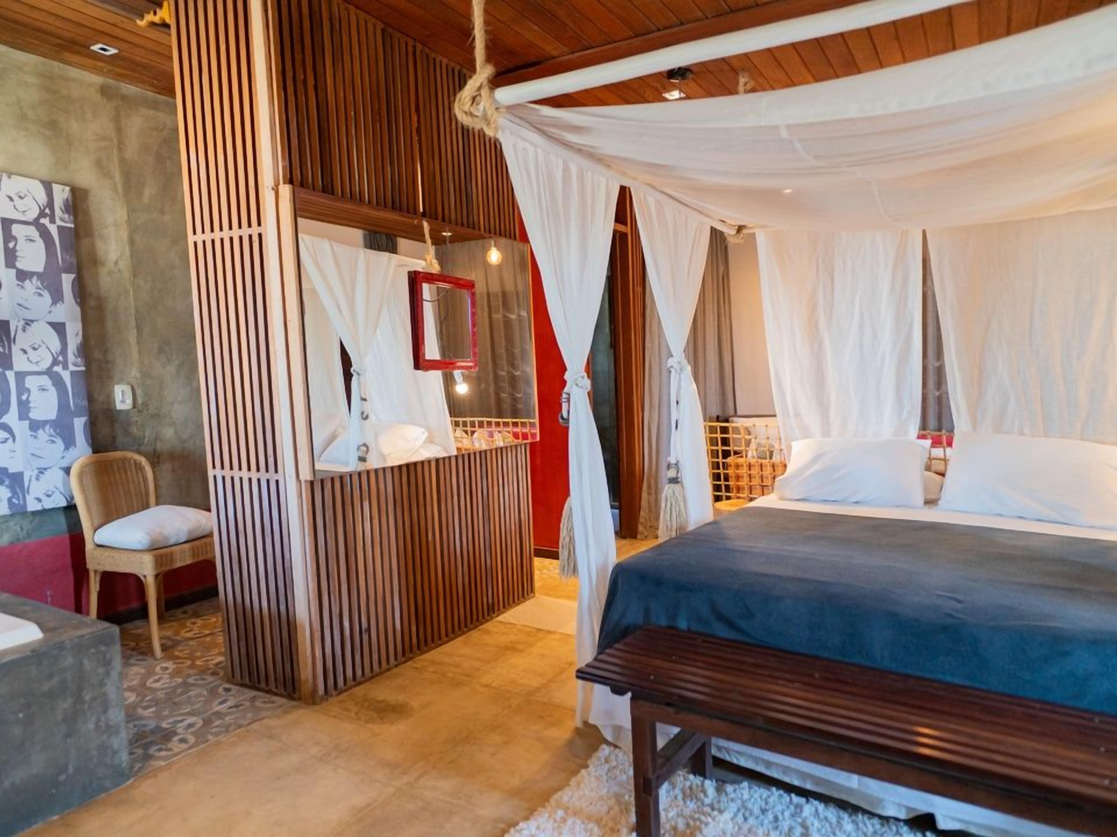 A bedroom with a canopy bed, a bedside table, a chair, and a mirror.