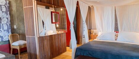 A bedroom with a canopy bed, a bedside table, a chair, and a mirror.