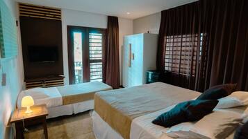 A hotel room with two beds, a TV, a desk with a lamp, and a window with curtains.