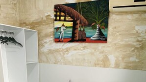 Una cama bien hecha con una colcha azul y blanca, un cabecero blanco y una pared con un cuadro de temática tropical.