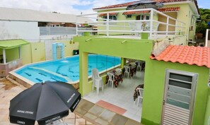Un espace piscine avec un bâtiment écologique, un coin salon couvert et une table avec des chaises.
