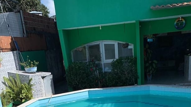 Una piscina con un diseño geométrico de azulejos, rodeada por un solárium con baldosas y un edificio verde al fondo.