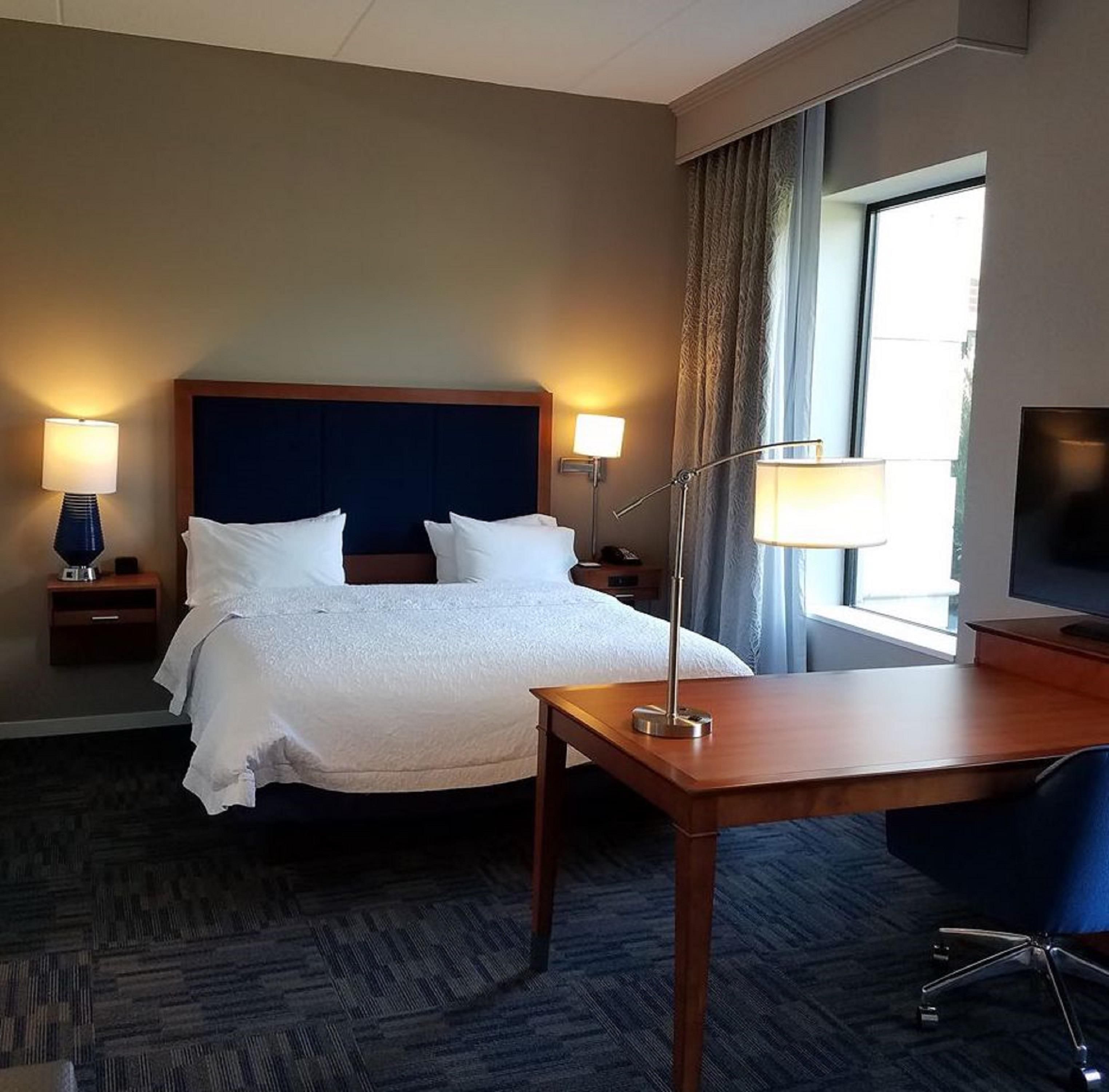 Een hotelkamer met een bed, nachtlampjes, een bureau, een stoel en een televisie.