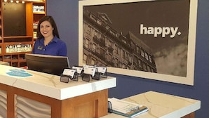 A hotel reception desk with a large 'happy.' poster on the wall, a counter with a computer, and a display of brochures.